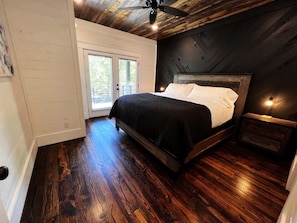 A bedroom with a wooden bed, a nightstand, a ceiling fan, and a view of the outdoors through a sliding door.