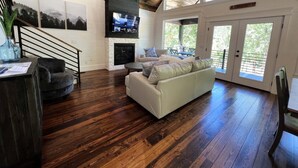 A spacious living room with a fireplace, a large TV mounted on the wall, and a staircase leading to an upper level. - Lakeside | Hot Tub | Kayaks | Fishing (MENA)