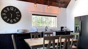 A kitchen with a large wall clock, wooden chairs, a window, and a refrigerator. - Lakeside | Hot Tub | Kayaks | Fishing (MENA)