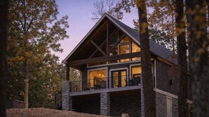 Une cabane en rondins à deux étages, avec des fondations en pierre, de grandes fenêtres et un balcon.