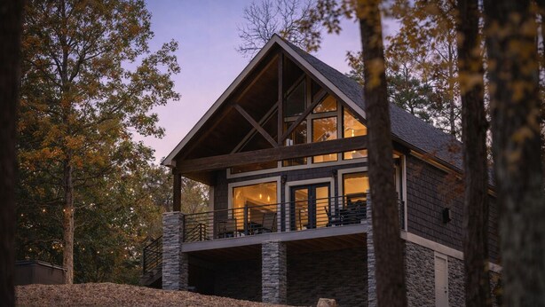 A two-story log cabin with a stone foundation, large windows, and a balcony. - Lakeside | Hot Tub | Kayaks | Fishing (MENA)