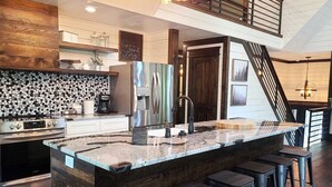 A modern kitchen with a large island, stainless steel appliances, and a wooden accent wall. - Lakeside | Hot Tub | Kayaks | Fishing (MENA)