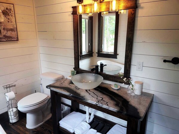 A bathroom with a white toilet, a glass bowl sink, and a wooden vanity.
