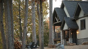 A cabin with a stone foundation and a steeply pitched roof, surrounded by trees and a pile of firewood. - Lakeside | Hot Tub | Kayaks | Fishing (MENA)