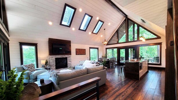 A spacious living area with a fireplace, a large sofa, and a dining area with a view of the outdoors. - Lakeside | Hot Tub | Kayaks | Fishing (MENA)