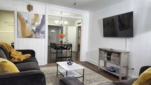 Un salon comprenant un canapé, une table basse et un téléviseur. Il y a également un coin repas avec des chaises et une table.