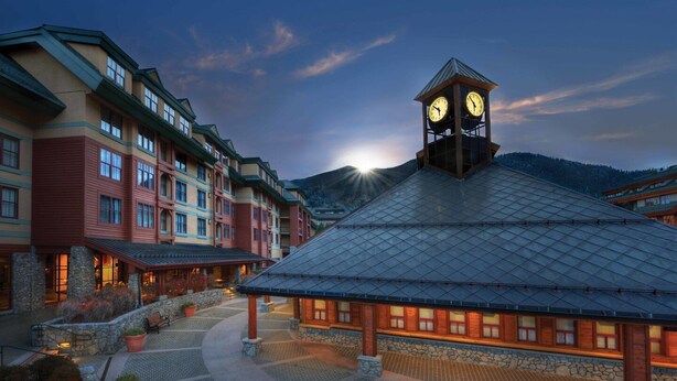 Un hotel con una torre de reloj central, un patio empedrado de piedra y varios edificios con grandes ventanales.