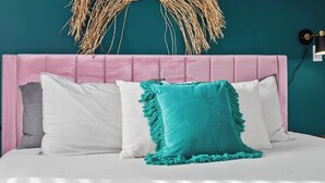 Un lit avec une tête de lit rose, une literie blanche et deux oreillers, dont un à rayures et l’autre de couleur turquoise.