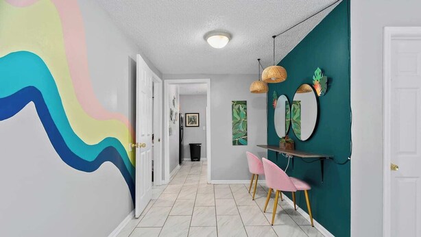 Un couloir agrémenté d’un mur aux motifs ondulés et colorés, d’un mur d’accent de couleur turquoise et d’une porte blanche au fond.