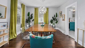 Une salle à manger avec une table en bois, des chaises transparentes, des rideaux verts et un lustre.