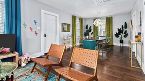 Un salon moderne avec un coin repas, comprenant un téléviseur, deux fauteuils en osier, un tapis coloré et une table à manger avec des chaises.
