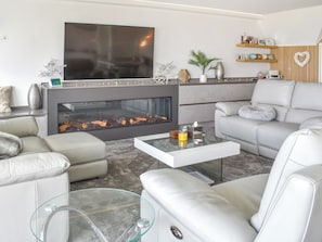 Ein modernes Wohnzimmer mit Kamin, Ledersofas, einem Glastisch und einem Flachbildfernseher.