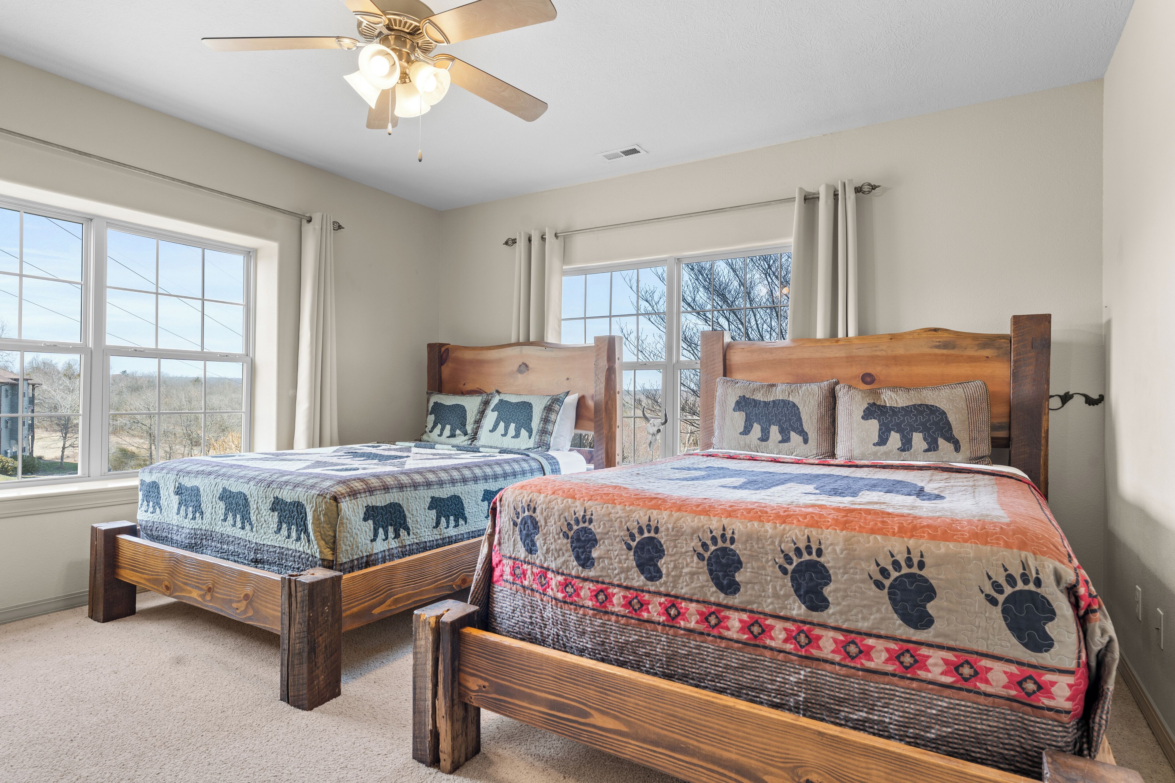 A bedroom with two wooden beds, large windows, and a ceiling fan.