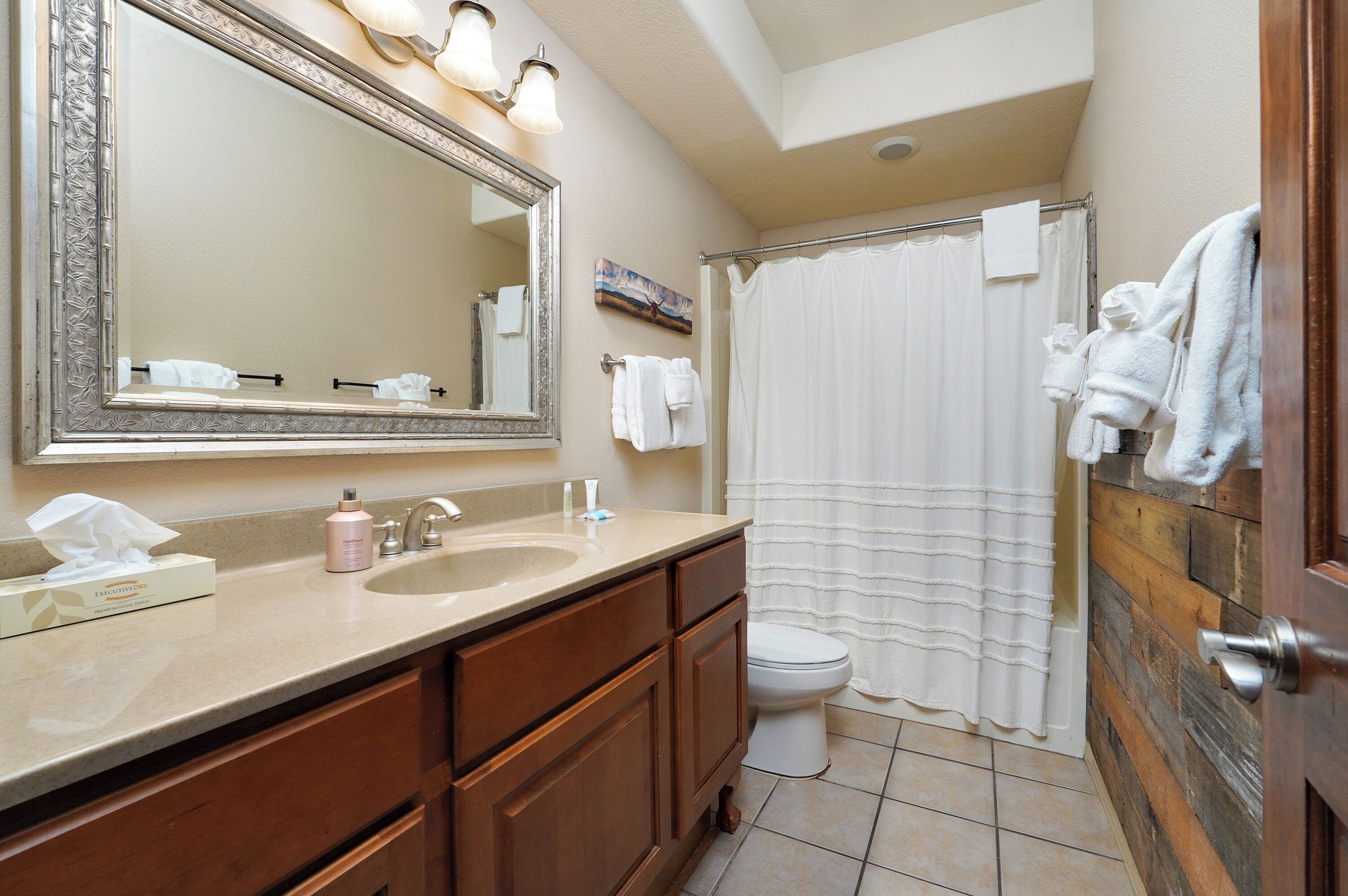 Une salle de bain avec un grand miroir, un lavabo avec un meuble-vasque, des toilettes et un rideau de douche.
