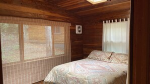 Een houten kamer met een bed, een raam met uitzicht en een plafondventilator.