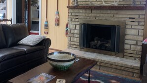 A cozy living room with a stone fireplace, a mounted deer head, and a leather couch. -  Cozy Cabin with river frontage yards from river launch for kayaking or fishing. (Cherokee Village)