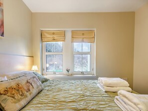 Une chambre à coucher avec un lit, une fenêtre avec des rideaux, une lampe de chevet et un tableau au mur.