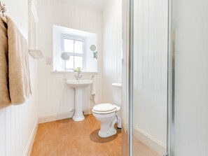 Une salle de bain avec un lavabo sur colonne, des toilettes, une douche à parois de verre et une fenêtre au-dessus du lavabo.