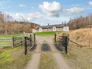 Une maison en pierre avec une allée bordée de gazon menant à une entrée fermée par un portail.