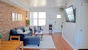 A living room with a brick wall, a sofa, a coffee table, and a TV mounted on the wall. - Private Patio + Parking + Near H Street & DC Attractions  Great for Families! (Washington)