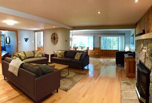 A spacious living room with a fireplace, wooden floors, and a large window providing natural light. - "Farm House" on Lake of Bays-Muskoka (Waterfront) (Huntsville)
