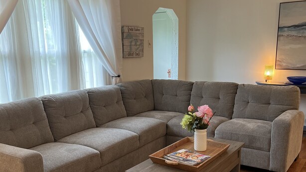 Ein Wohnzimmer mit einem Ecksofa, einem Couchtisch aus Holz mit Zeitschriften und einer Vase mit Blumen.