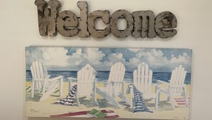 Ein 'Willkommen'-Schild und ein Bild von Strandstühlen an der Wand.