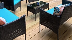 Eine Terrasss mit Korbmöbeln und einem Glastisch, umgeben von Bäumen.