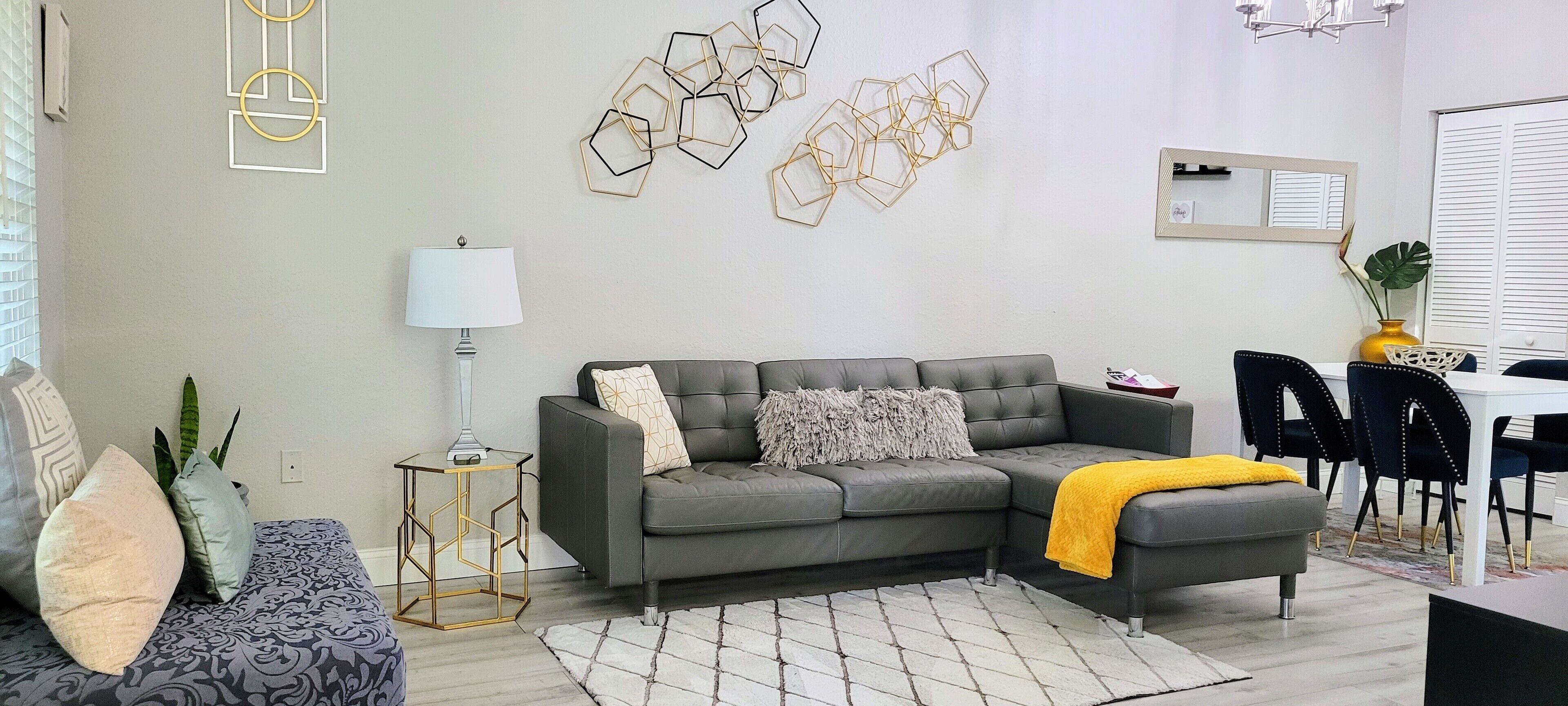 A modern living room with a grey sectional sofa, a patterned armchair, a geometric side table, and a yellow throw blanket.
