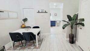 Una cocina moderna con armarios blancos, encimera negra y un comedor con mesa blanca y sillas negras.