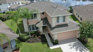 A two-story house with a sloped roof, a covered front porch, and a small front yard with a palm tree. - 5 bedroom lakefront home w/ large private pool & spa - Close to WDW & Universal (Kissimmee)