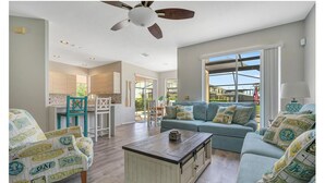 A spacious living room with a sofa, chairs, and a coffee table. There is a ceiling fan, a window with a view, and a kitchen area in the background. - 5 bedroom lakefront home w/ large private pool & spa - Close to WDW & Universal (Kissimmee)