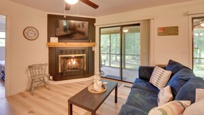 Una sala de estar con chimenea, ventilador de techo, televisor y un gran ventanal.