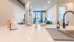 A modern kitchen with a central island, a dining area with chairs, and a view of the city through large windows. - Emerald Escape with Free Parking & 2 baths. 5 beds+Sleeps 8!  ✨20% OFF 7 days✨ (East Orange)