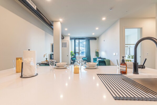 A modern kitchen with a central island, a dining area with chairs, and a view of the city through large windows.