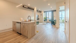 A modern kitchen with a dishwasher, a central island, and a dining area with a green sofa and a small table. - Emerald Escape with Free Parking & 2 baths. 5 beds+Sleeps 8!  ✨20% OFF 7 days✨ (East Orange)