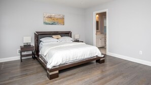 Une chambre à coucher avec un lit en bois, deux tables de chevet, une commode, un tableau au mur et un couloir menant à une salle de bain.