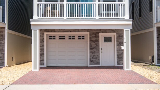 Une maison de ville à deux étages avec un garage à l’avant, un balcon à l’étage supérieur et une façade en briques.
