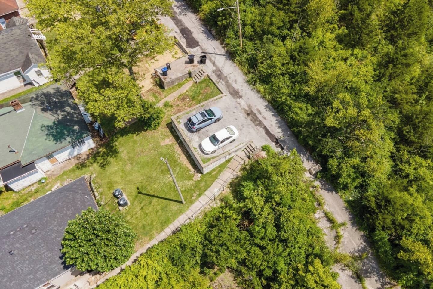 An aerial view of a residential area with a parking lot, a basketball court, and a dense green forest.