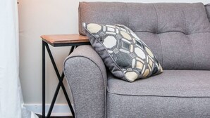 A grey sofa with a patterned pillow, a small wooden side table, and a wall-mounted lamp. - This house is a 2 bedroom(s), 1 bathrooms, located in Frankfort, KY. (Frankfort)