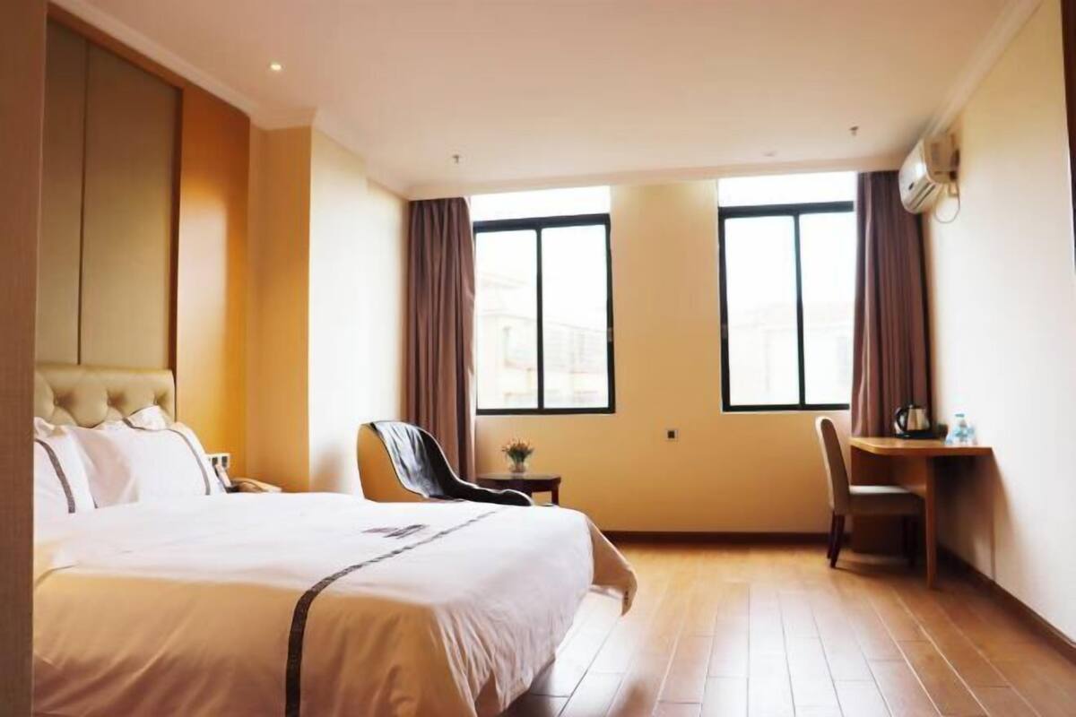 A hotel room with a large bed, a desk, and two windows.