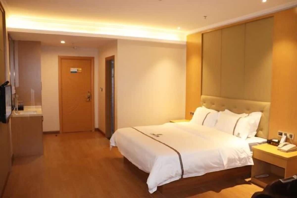 A hotel room with a large bed, bedside tables, a wooden floor, and a door.
