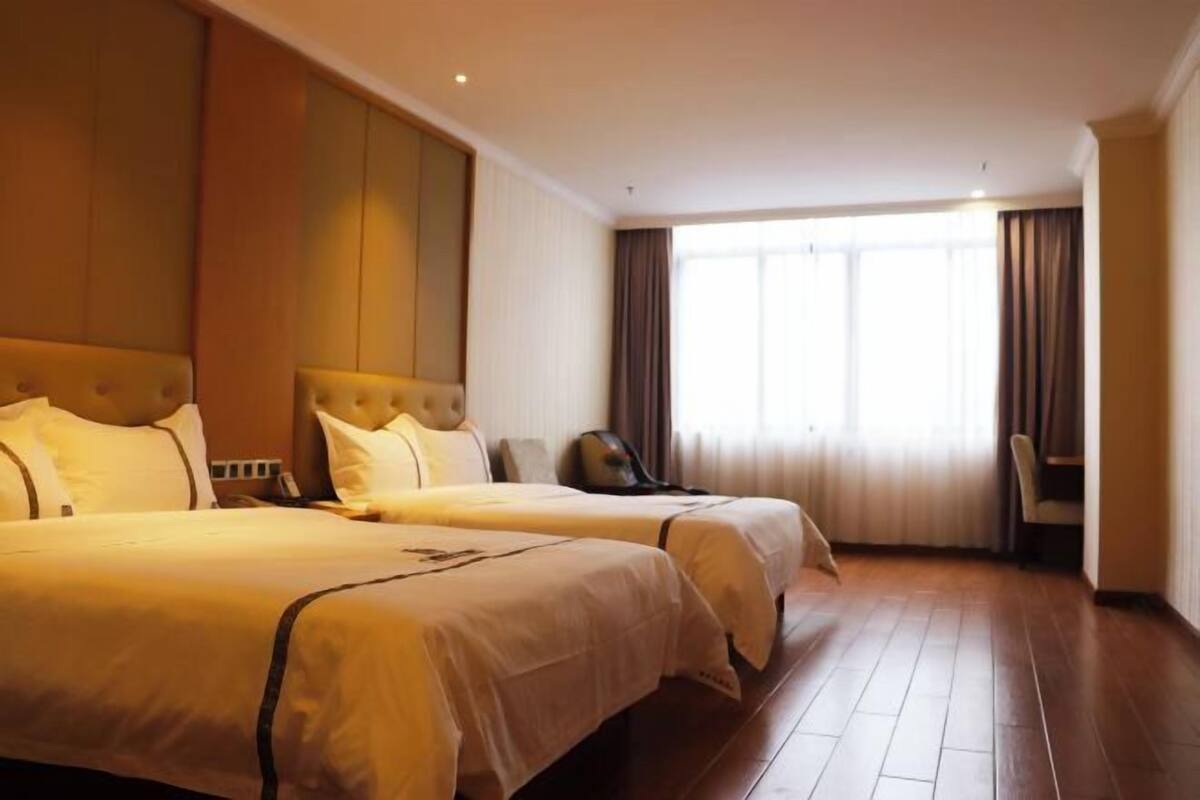 A hotel room with two beds, a large window with curtains, and a wooden floor.