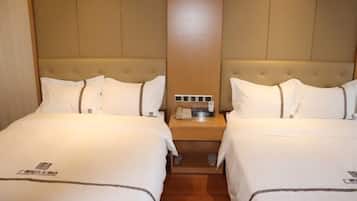 A hotel room with two beds, a wooden headboard, a nightstand with a phone and a lamp, and a small table between the beds.