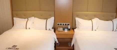 A hotel room with two beds, a wooden headboard, a nightstand with a phone and a lamp, and a small table between the beds.