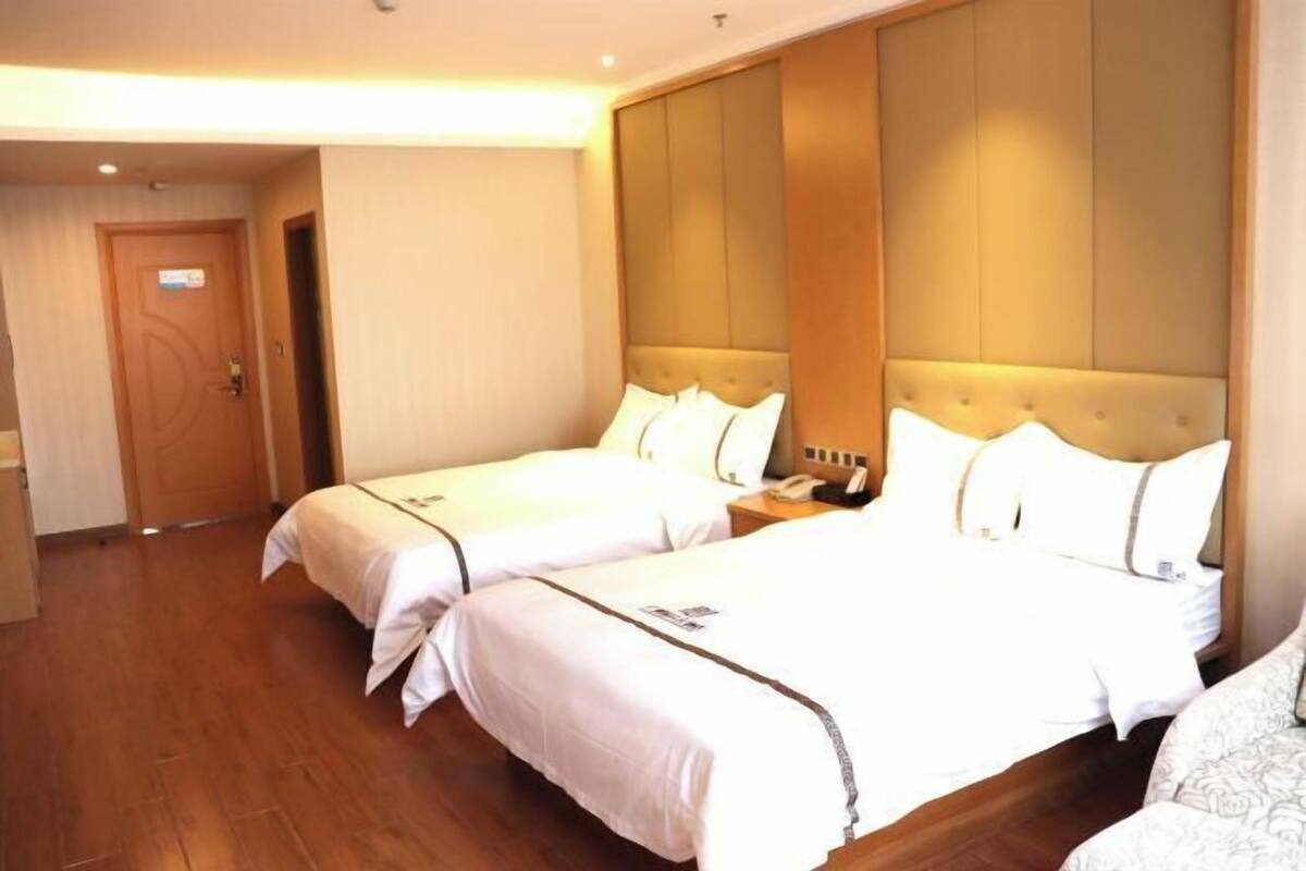 A hotel room with two beds, a wooden floor, a large padded headboard, and a door with a sign.