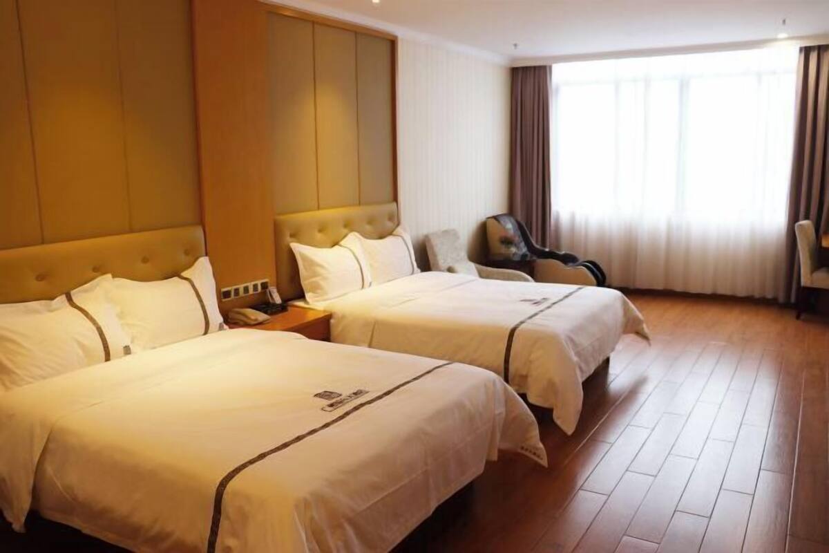 A hotel room with two beds, a desk, a chair, and a large window with curtains.