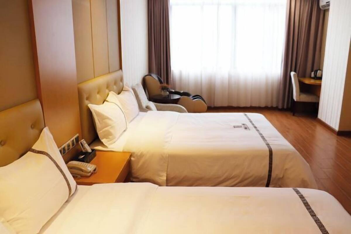 A hotel room with two beds, a chair, a desk, and a window with curtains.