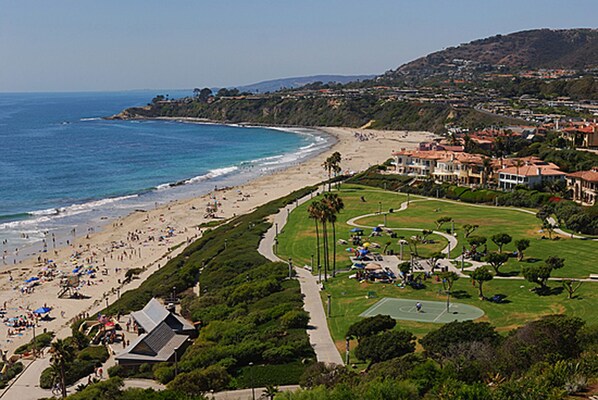 A coastal area with a beach, a tennis court, and residential buildings.