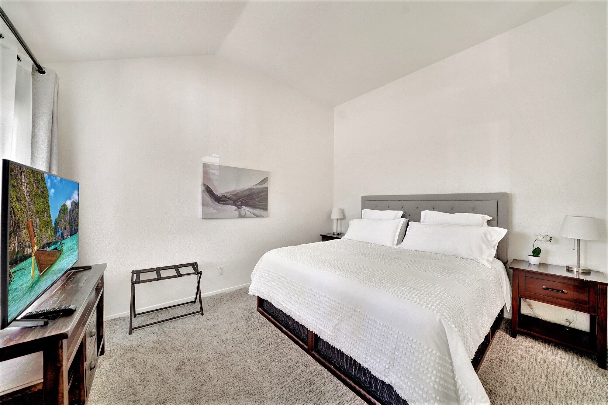 A bedroom with a large bed, a TV on a wooden dresser, a small table, and a wall-mounted shelf.